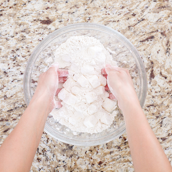 Preparation step for flakey all-butter pie crust - Hands coating butter cubes with flour