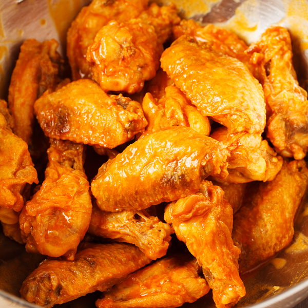 Preparation step for baked buffalo wings - wings coated with buffalo sauce in bowl.