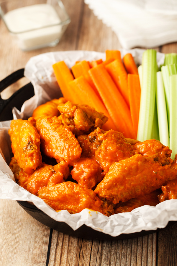 Baked buffalo wings with carrots and celery sticks on serving dish.