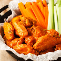 Baked buffalo wings with carrots and celery sticks on serving dish.