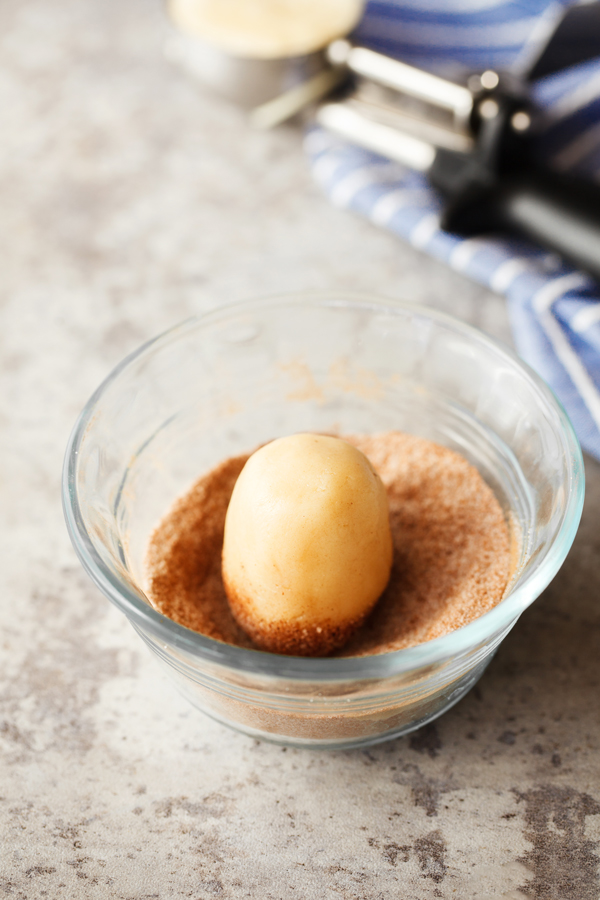 Preparation step for snickerdoodle cookies - dough ball being coated in cinnamon and sugar mixture