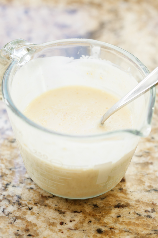 Preparation step for Martino's Bakery original tea cakes - buttermilk in glass measuring cup with spoon